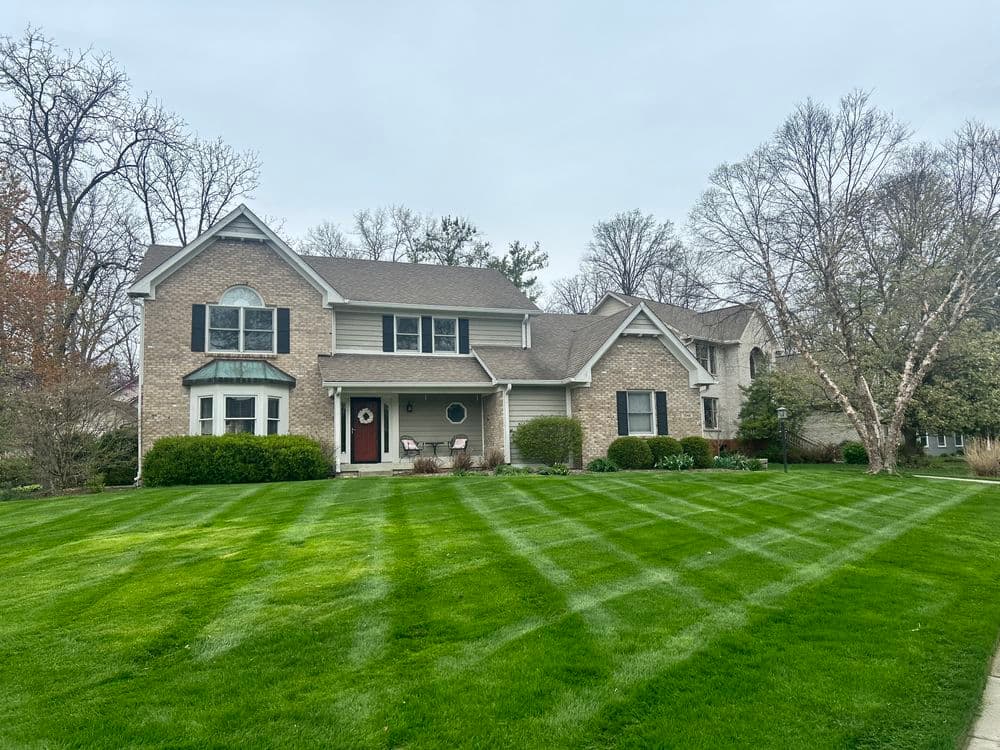 Spacious brick house with manicured lawn and neat landscaping on a cloudy day.